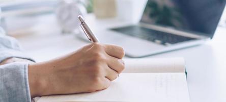 mulher escrevendo no caderno de planejamento enquanto usa o laptop para trabalhar foto