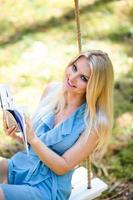 lindo loiro mulher dentro azul vestir lendo uma livro em uma balanço foto