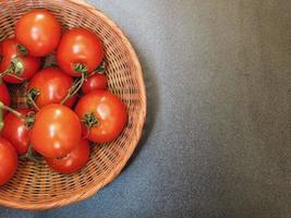 tomates em uma cesta de vime em um fundo escuro de mesa foto
