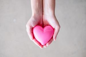 mão feminina segurando um coração rosa, um conceito de saúde, medicina e caridade foto
