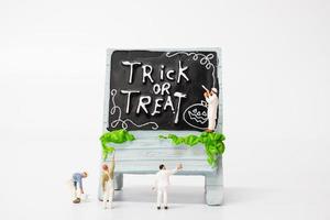 pessoas em miniatura colorindo decorações de adereços de festa de halloween em um fundo branco, conceito de festa de halloween foto