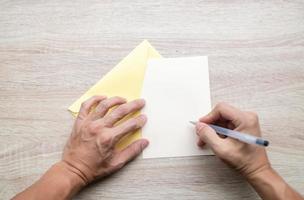 mãos masculinas escrevendo em um cartão vazio em uma mesa de madeira foto