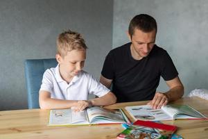 uma fofa Garoto é sentado às a mesa com dele Papai e assistindo uma livro sobre cobras foto