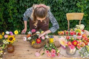 uma fofa florista menina coleta uma ramalhete dentro uma cesta do outono flores em dela Área de Trabalho foto