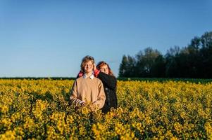 dois meninas ficar de pé dentro uma colza campo dentro Primavera e Veja às a Sol foto