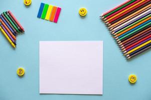 uma conjunto do brilhante papelaria Itens em uma azul fundo. colori lápis e branco papel foto