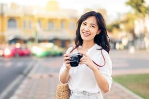 feliz juventude ásia mulher pessoa com Câmera viaja rua cidade viagem em lazer fim de semana. jovem hipster menina fêmea turista passeios turísticos verão urbano Bangkok destino estilo de vida conceito. foto