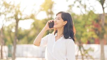 retrato lindo jovem ásia mulher com inteligente Móvel telefone por aí ao ar livre natureza Visão dentro uma ensolarado verão dia foto