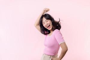 retrato lindo jovem ásia mulher feliz sorrir dança com punho acima vitória gesto expressão alegre dela sucesso realização contra Rosa pastel estúdio fundo. mulher dia celebração conceito. foto