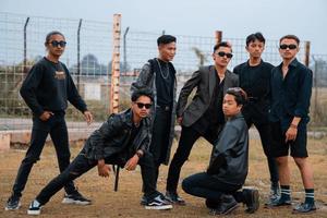 uma grupo do Adolescência Rapazes dentro Preto roupas posando muito galantemente com seus amigos dentro uma campo foto