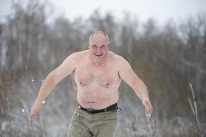 a adulto homem é endurecido de neve em uma inverno dia. homem com neve chuveiros para endurecer dele corpo foto