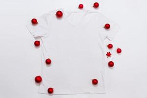 feche a camiseta branca modelo em branco com espaço de cópia e o conceito de férias de natal. t-shirt de maquete de vista superior e decorações vermelhas de feriados em fundo branco. feliz ano novo acessórios. roupa de natal foto