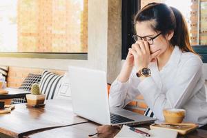 ásia empresária tendo dor de cabeça enquanto trabalhando em dela computador portátil dentro escritório. uma dor de cabeça é dor ou desconforto dentro a cabeça ou face área. foto