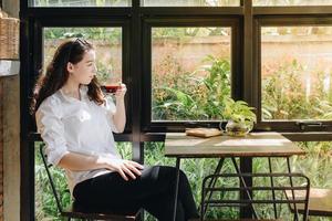 retrato do jovem misturado raça mulher sentado dentro a moderno interior escritório enquanto bebendo uma quente café. foto