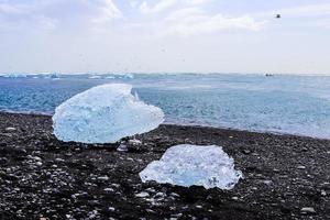 praia de diamante na islândia com icebergs azuis derretendo na areia preta e gelo brilhando com a luz do sol. foto