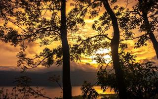 dourado hora pôr do sol panorama com lago Visão geral e silhueta do árvores foto