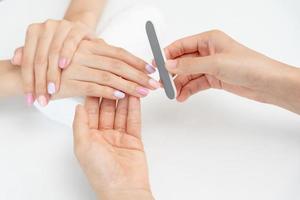 mulher recebe serviço de atendimento por manicure esteticista profissional no centro de spa. salão de beleza de unhas usa lixa de unha para tratamento de esmalte. manicure faz cliente de unha bonita. tratamento de spa para cuidados com o corpo foto