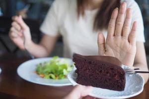 a menina é empurrando a chocolate bolo fora. e escolher para comer salada legumes colocada dentro frente. a objetivo é para perder peso e comer saudável Comida. foto