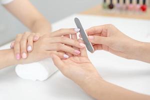 mulher recebe serviço de atendimento por manicure esteticista profissional no centro de spa. salão de beleza de unhas usa lixa de unha para tratamento de esmalte. manicure faz cliente de unha bonita. tratamento de spa para cuidados com o corpo foto