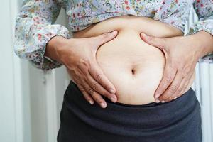 a mulher asiática com excesso de peso usa a mão para espremer a barriga gorda, o sobrepeso e a obesidade. foto