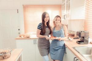 uma feliz jovem lésbica casal segurando uma pizza dentro a cozinha. a conceito do feito em casa Comida e lgbt relacionamentos. família e diversidade conceito. lgbt. caloroso tom. foto