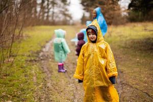 Garoto dentro amarelo capa de chuva contra mãe e crianças dentro a floresta depois de chuva dentro capas de chuva junto. foto