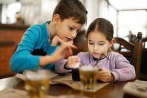 irmão com irmã jogar dentro Smartphone junto, enquanto comer dentro restaurante. foto