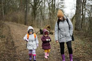 mãe e dois filhas com mochilas caminhando ao longo a floresta estrada junto. foto