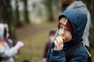 Garoto com mochila comendo croissant dentro a floresta. foto