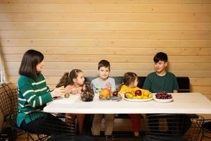 mãe com quatro crianças comer frutas dentro de madeira país casa em fim de semana. foto