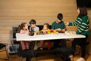 mãe com quatro crianças comer frutas dentro de madeira país casa em fim de semana. mãe cortes a amarelo Dragão fruta. foto