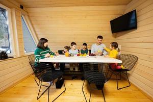 família com quatro crianças comer frutas dentro de madeira país casa em fim de semana. foto