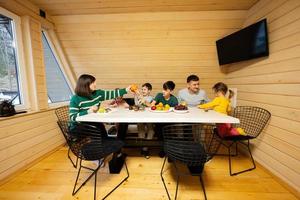 família com quatro crianças comer frutas dentro de madeira país casa em fim de semana. foto