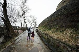 mãe e meninas andar acima a molhado caminho para a antigo medieval castelo fortaleza dentro chuva. foto