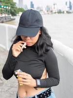 retrato mulher menina adolescente jovem Ásia 1 pessoa vestindo uma chapéu e grandes Preto cabelo vestindo uma Preto camisa mão aguarde fumar cigarro branco cor em pé ao ar livre de a parede ao ar livre foto