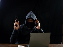 hacker espião homem uma pessoa com capuz preto sentado em uma mesa olhando computador laptop usado segurança de ataque de senha de login para circular dados digitais no sistema de rede da internet, fundo escuro noturno.