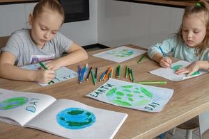 crianças desenhar a planeta terra com lápis e ponta de feltro canetas em álbum folhas para terra dia às seus casa mesa. a conceito do protegendo a ambiente, Paz em terra. foto