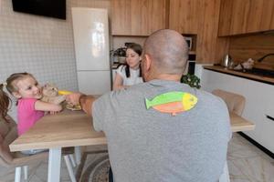 a família durante café da manhã dentro a cozinha em a primeiro do abril piadas e Gravetos papel peixe em cada outros costas. engraçado família piadas, tradições, abril tolo dia celebração foto