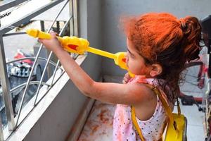 doce pequeno indiano menina jogando cores em holi festival, segurando pichakaree cheio do cores, holi festival celebrações dentro Délhi, Índia foto