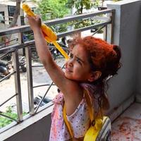 doce pequeno indiano menina jogando cores em holi festival, segurando pichakaree cheio do cores, holi festival celebrações dentro Délhi, Índia foto
