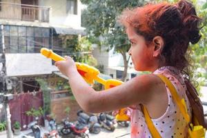 doce pequeno indiano menina jogando cores em holi festival, segurando pichakaree cheio do cores, holi festival celebrações dentro Délhi, Índia foto