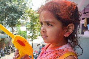 doce pequeno indiano menina jogando cores em holi festival, segurando pichakaree cheio do cores, holi festival celebrações dentro Délhi, Índia foto