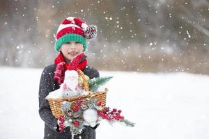 feliz Garoto dentro uma listrado Natal chapéu com Natal brinquedos e decorações debaixo a queda de neve. foto