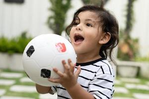 fofa pequeno Garoto jogando futebol com bola ao ar livre em futebol campo foto