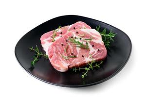 peças do carne de porco carne com alecrim e Tomilho folhas em Preto prato em branco fundo, foto