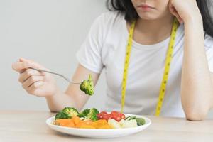 dieta dentro entediado. fechar-se brócolis infeliz lindo ásia jovem mulher, menina em fazer dieta, mão segurando garfo dentro salada placa, não gostar ou cansado com comer fresco legumes. nutrição do saudável Comida Boa gosto foto