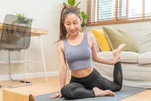 ajustar, desportivo ásia jovem mulher dentro roupa de esporte sentado em chão, exercício em esteira, assistindo conectados Treinamento videos em tábua dentro vivo quarto às lar. exercite-se fitness, pilates para bem-estar, saudável Cuidado. foto