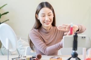 beleza blogueiro, ásia jovem mulher, menina vlogger Maquiagem face, mostrando, avaliações cosméticos produtos enquanto gravação vídeo, tutorial para compartilhar em social meios de comunicação. o negócio conectados influenciador em Smartphone. foto