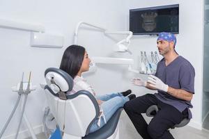 masculino dentista falando para hispânico fêmea paciente durante consulta foto
