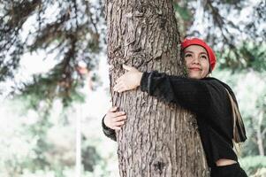 contente jovem mulher abraçando uma ampla árvore com uma feliz expressão com cópia de espaço foto